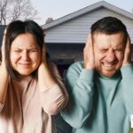 Couple covering their ears in front of a Texas home, symbolizing the stress of foreclosure and the need for urgent housing solutions